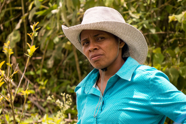 Photograph of a woman with a serious look on her face. Her brows are furrowed and she looks directly into the camera. She wears a cowboy hat and a collared shirt. This is Denia, who founded a group of youth as farmer-researchers.